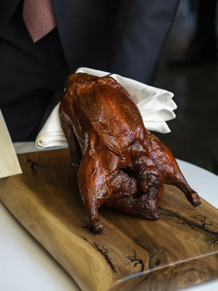Roasted whole duck on wooden board held by server in suit with white napkin