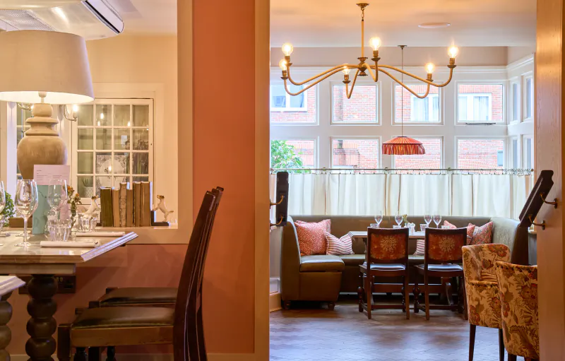 Dining area at The White Horse, Dorking, UK: wooden table with lamp and menu, view through doorway to chandelier-lit dining room with sofa and set table