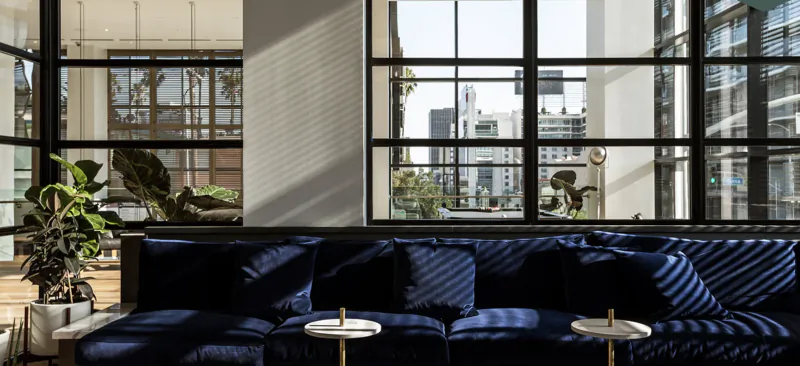 Modern hotel lobby with navy blue velvet sofa, round side tables, and large windows overlooking Hollywood cityscape