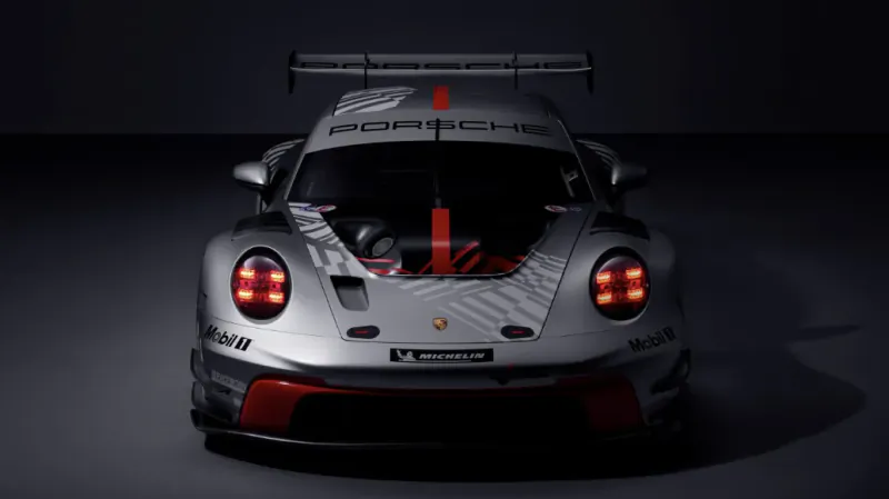 Rear view of silver Porsche 911 race car with large rear wing, red taillights, and sponsor logos in dark studio