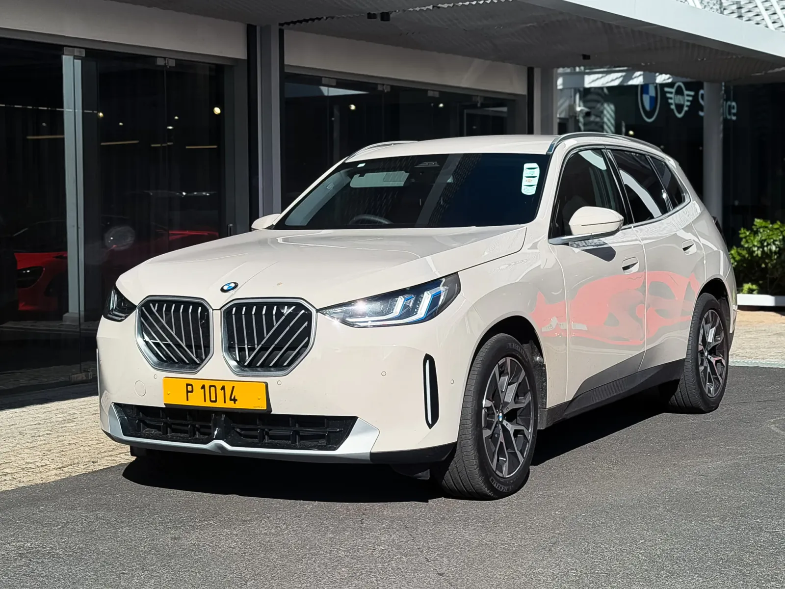 White BMW X5 SUV parked in front of a BMW dealership with yellow European license plate