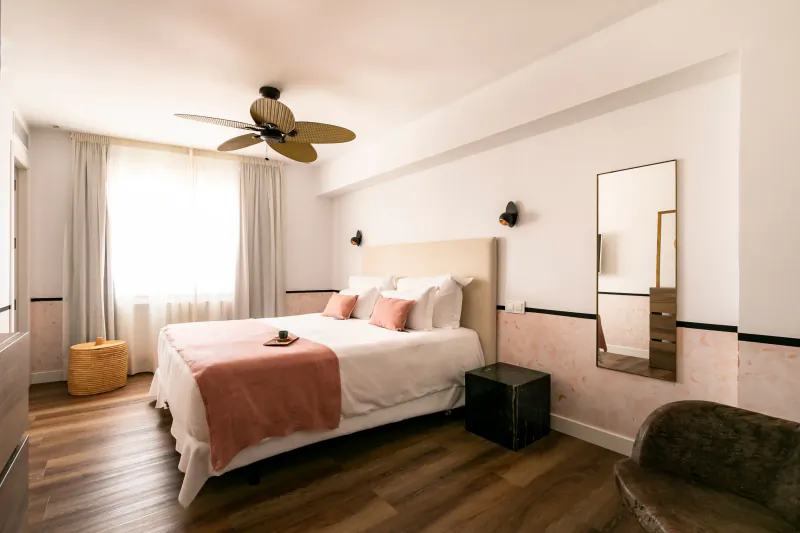 Bright modern bedroom with beige bed, pink throw, ceiling fan, full-length mirror, and window with sheer curtains