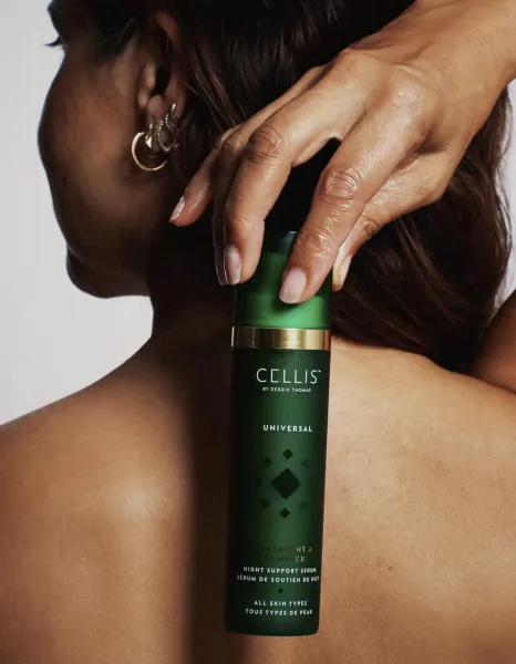 Woman holding a green Cellis Universal night support serum bottle against her shoulder