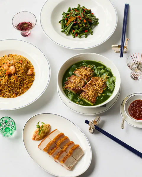Overhead view of a Chinese meal with green bean stir-fry, shrimp fried rice, pork belly slices, and green soup with crispy pork.