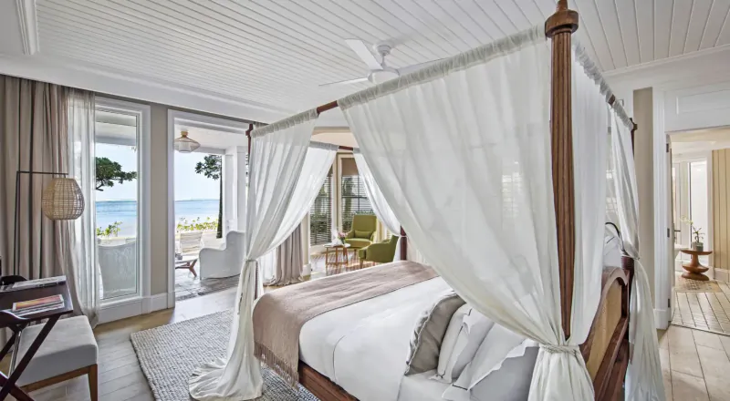 Luxury four-poster bed with white canopy in a bright beachfront hotel suite overlooking the ocean