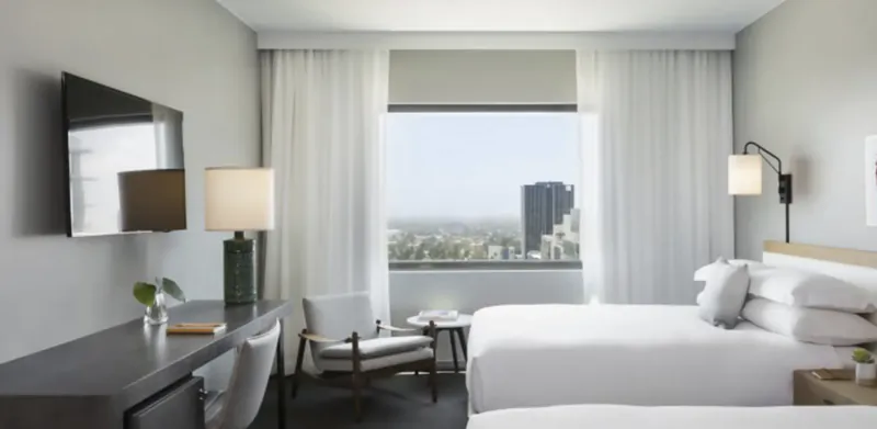 Modern hotel room with a large bed, city view window, wall-mounted TV, and seating area