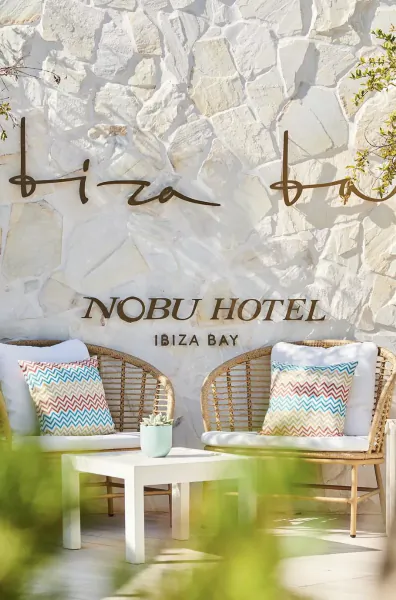 Nobu Hotel Ibiza Bay entrance with two wicker chairs and 'Ibiza Bay' sign on stone wall