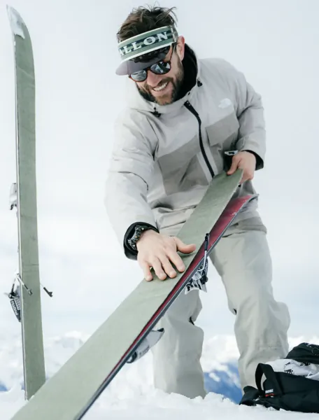 Smiling man in winter gear holding skis on snowy mountain slope