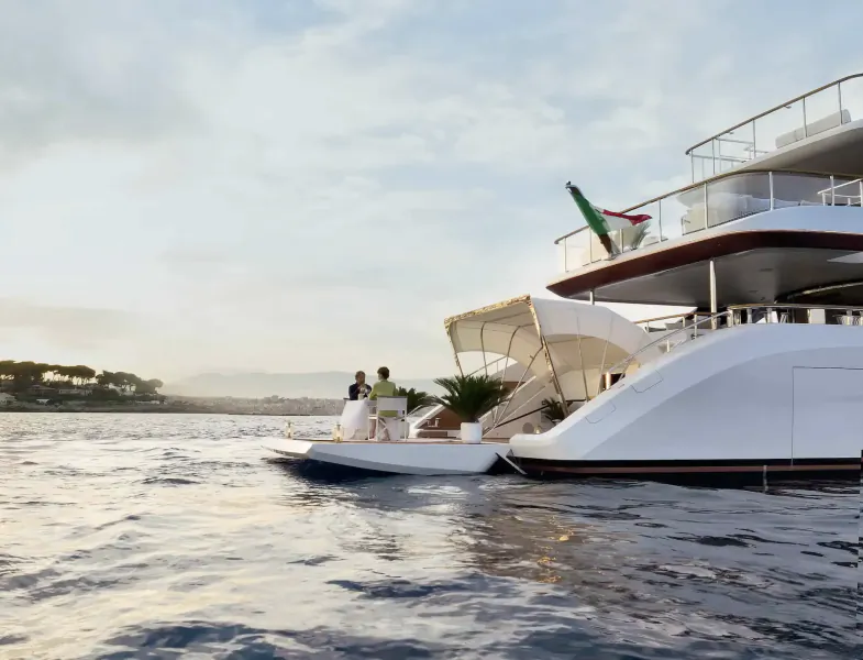 White luxury yacht Sundance with tender boat alongside on calm water, Italian flag flying from upper deck