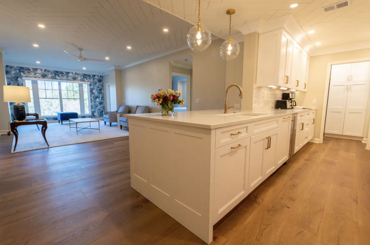 Modern open kitchen with white island, gold faucet, and pendant lights overlooking living room with hardwood floors