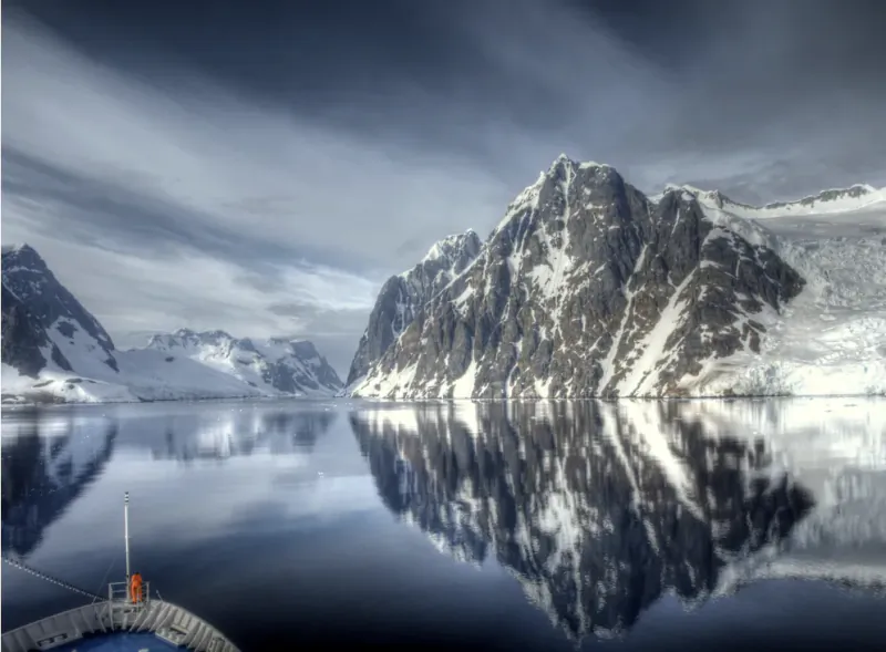 Snow-capped mountains reflected in calm Antarctic waters, viewed from a luxury expedition ship deck