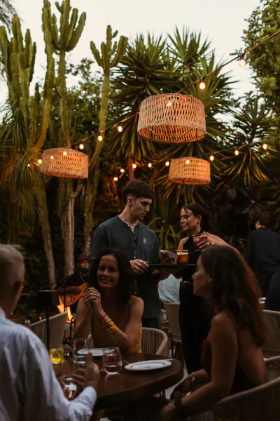 Evening gathering at La Finca Plaza Ibiza: friends dining outdoors under woven pendant lights and tall cacti