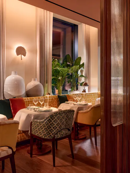 Elegant restaurant interior with patterned upholstered chairs, white tablecloths, and warm lighting at La Môme London
