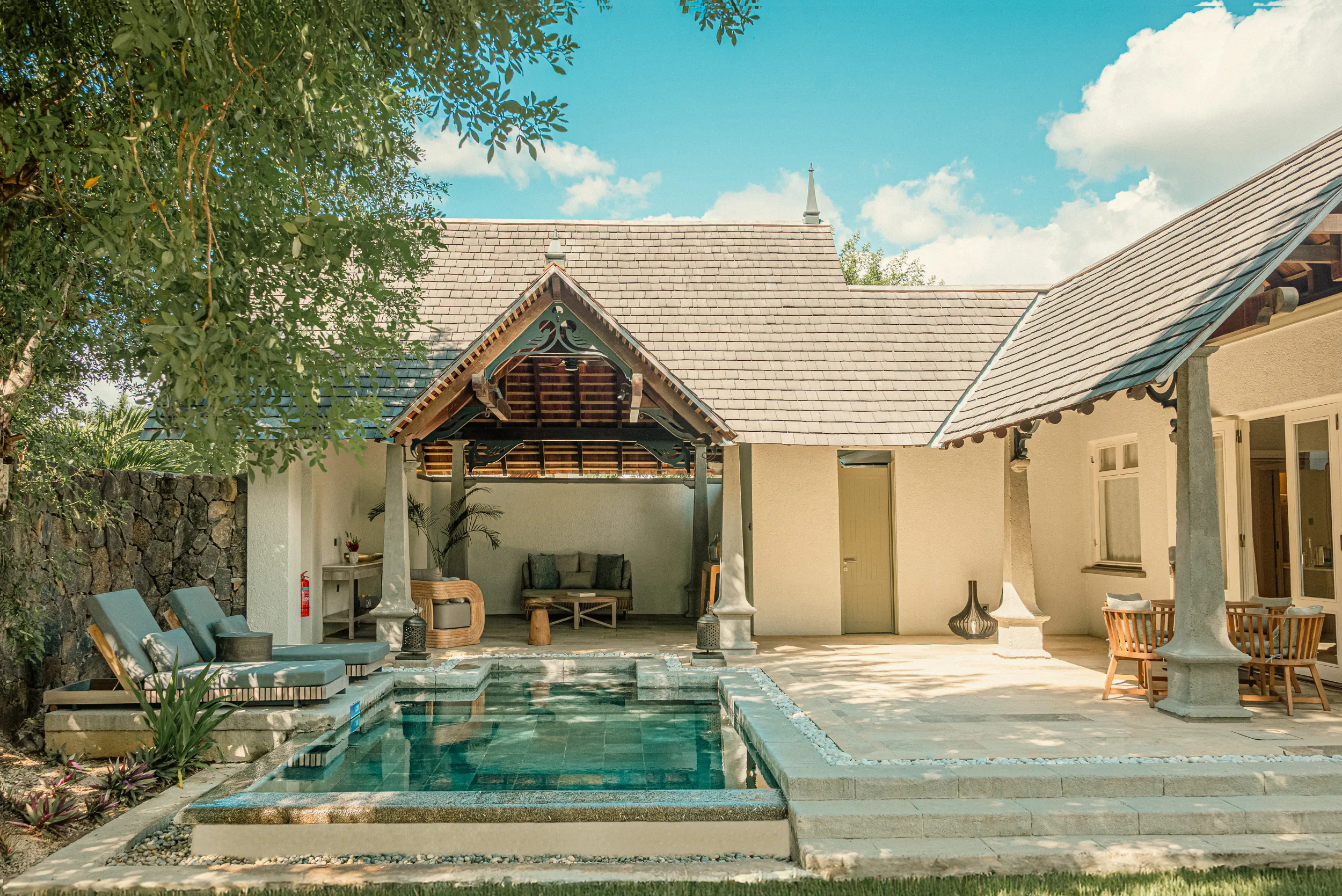 Luxury resort villa with private pool, lounge chairs, and traditional thatched roof under blue sky