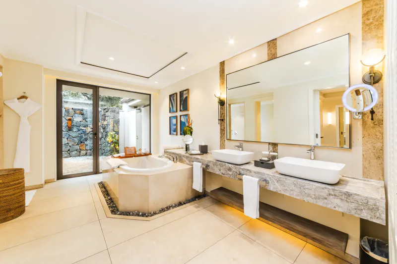 Luxury hotel bathroom with freestanding bathtub, double marble vanity sinks, large mirror, and open doors to a private garden