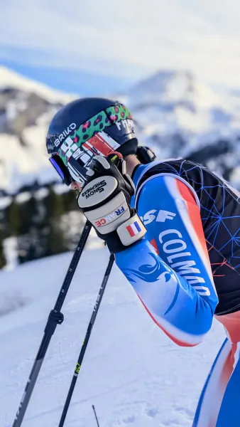 Skier in blue, red and black suit adjusts goggles on snowy mountain slope