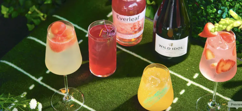 Four colorful cocktails and two bottles of Everleaf and Wild Idol on a green turf table