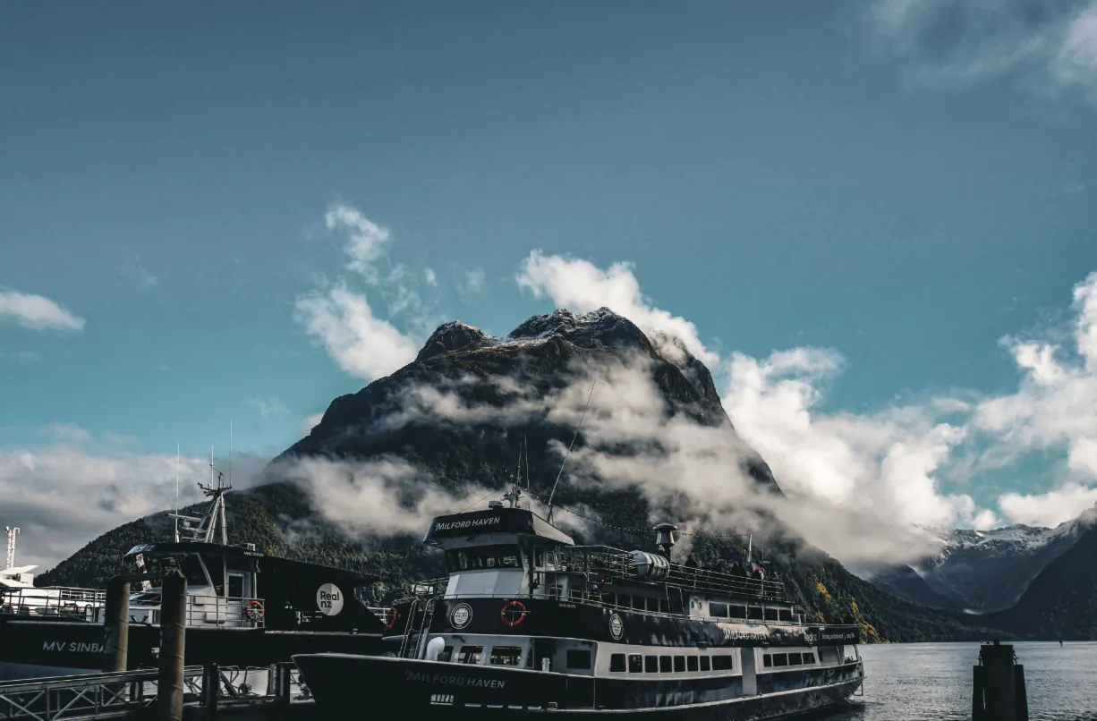 Ferry docked at pier with misty mountain backdrop under blue sky