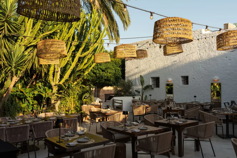 La Finca Plaza Ibiza outdoor restaurant patio with woven lamps, tables set for dinner, and lush tropical plants