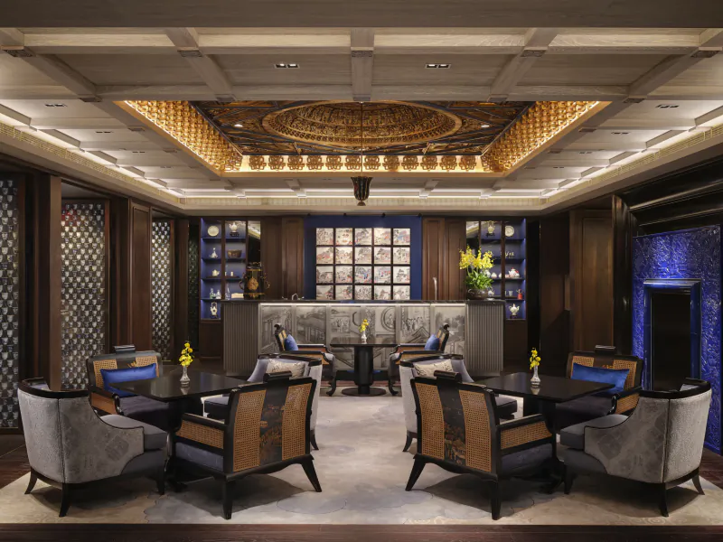 Elegant luxury lounge with ornate gold ceiling, dark wood paneling, blue accents, and plush armchairs arranged around tables
