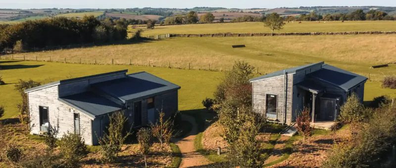Two modern grey glamping cabins with dark roofs in a rural field near Moreton-in-Marsh