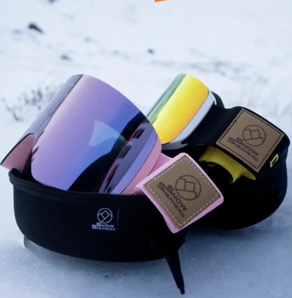 Snow Shepherd ski goggles with iridescent purple and yellow lenses in a black case on snow