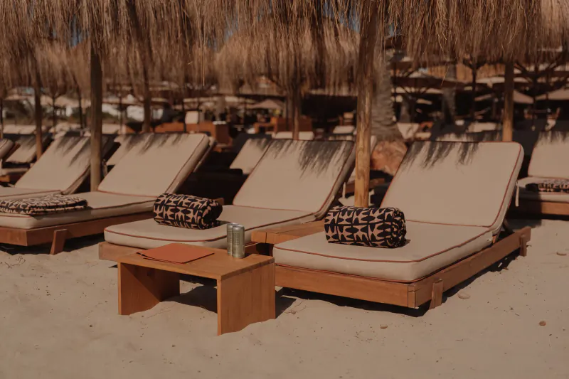Rows of beige lounge chairs with patterned cushions under thatched umbrellas on a sandy beach