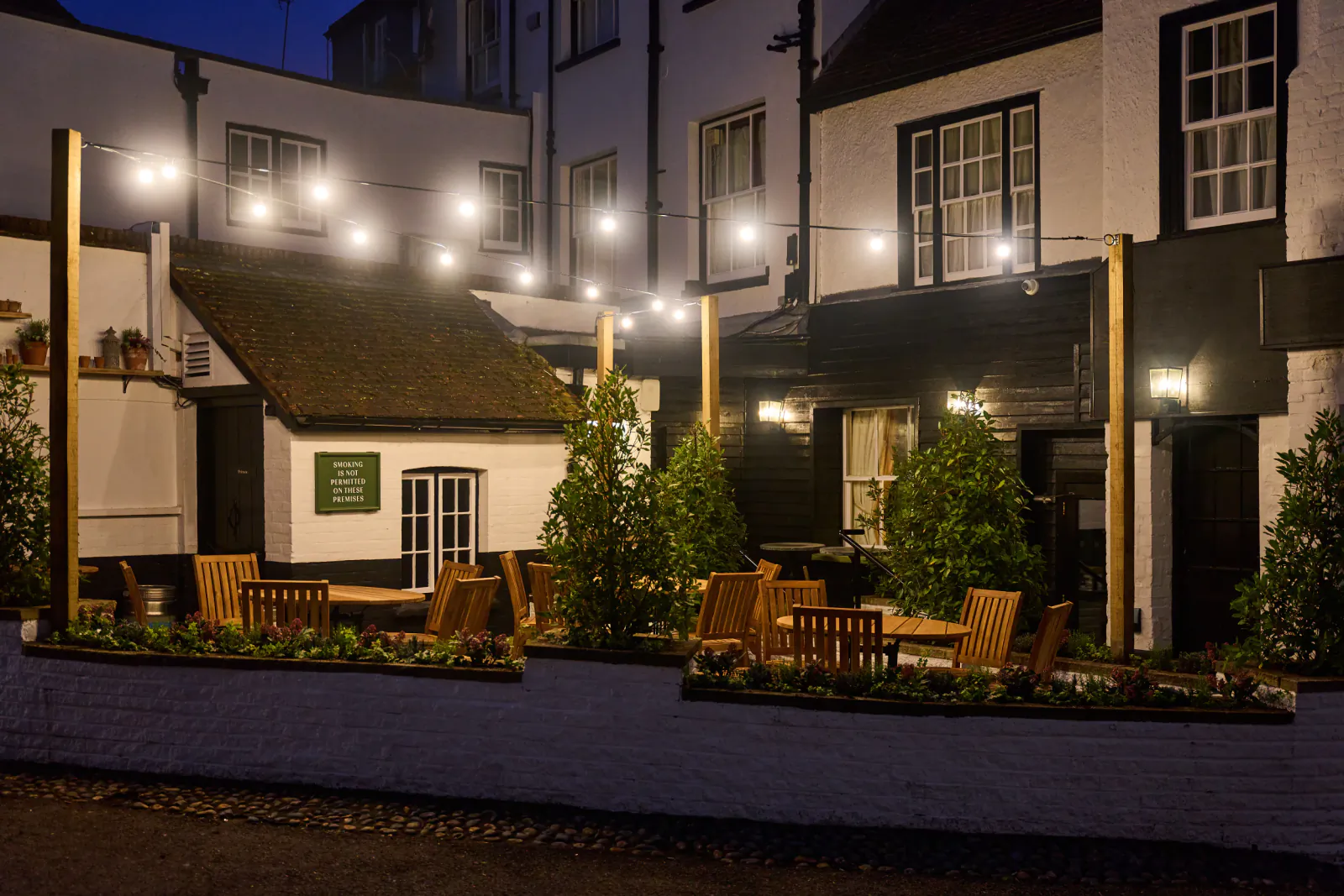 Evening view of The White Horse pub in Dorking with outdoor seating, string lights, and white buildings