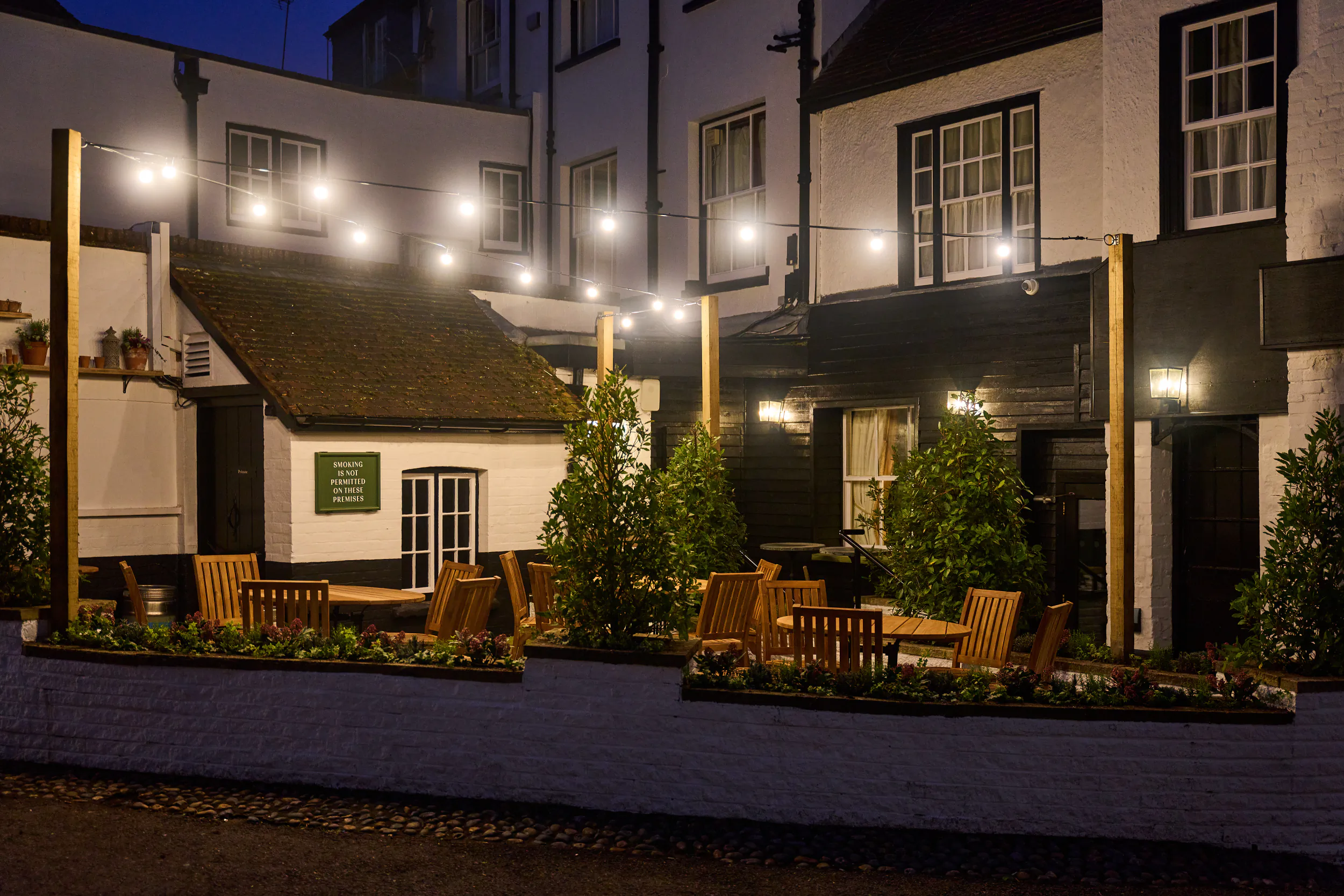 Evening view of The White Horse pub in Dorking with outdoor seating, string lights, and white buildings