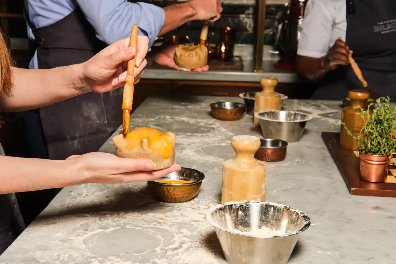 Hands drizzling caramel sauce over a small pie at a pie masterclass