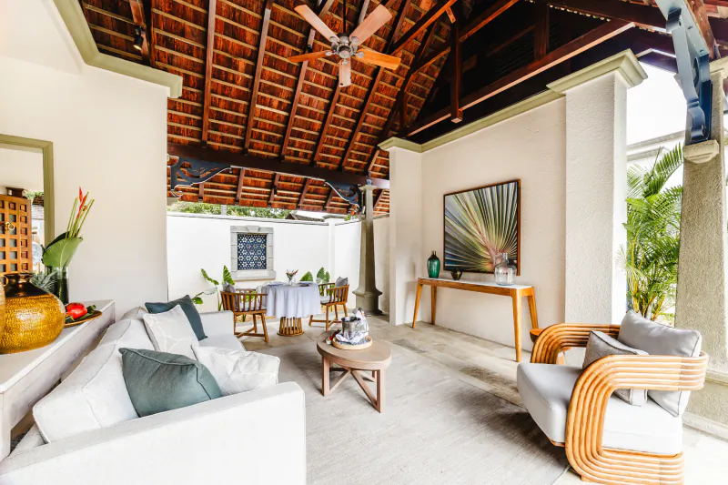 Luxury resort lounge with white sofas, striped armchair, wooden ceiling fan, and outdoor dining area