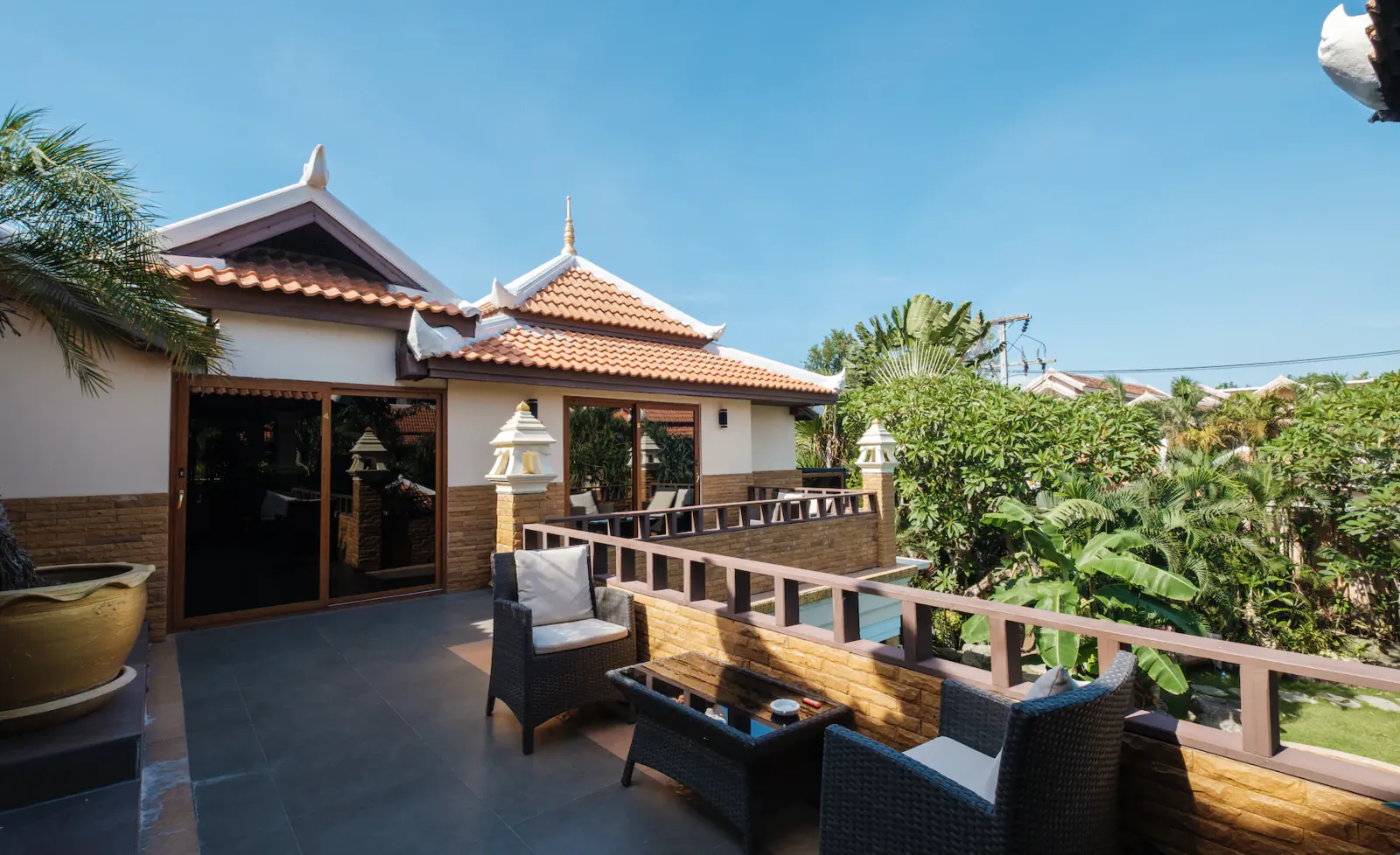 Luxury villa balcony with wicker seating, overlooking tropical gardens and a pool under a clear blue sky