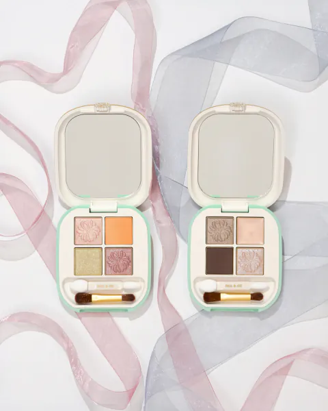 Two open Paul & Joe eyeshadow palettes with four floral-embossed shades each, mirrors, and dual-ended applicators on pink and blue ribbons