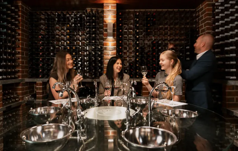 Four people tasting wine at a bar in a brick-walled wine cellar with bottles on shelves