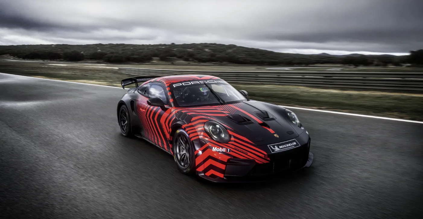 Red and black Porsche 911 race car with sponsor logos driving on a racetrack
