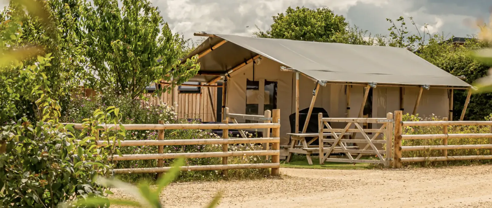 Luxury glamping tent with wooden deck and fence, surrounded by greenery at Moreton-in-Marsh