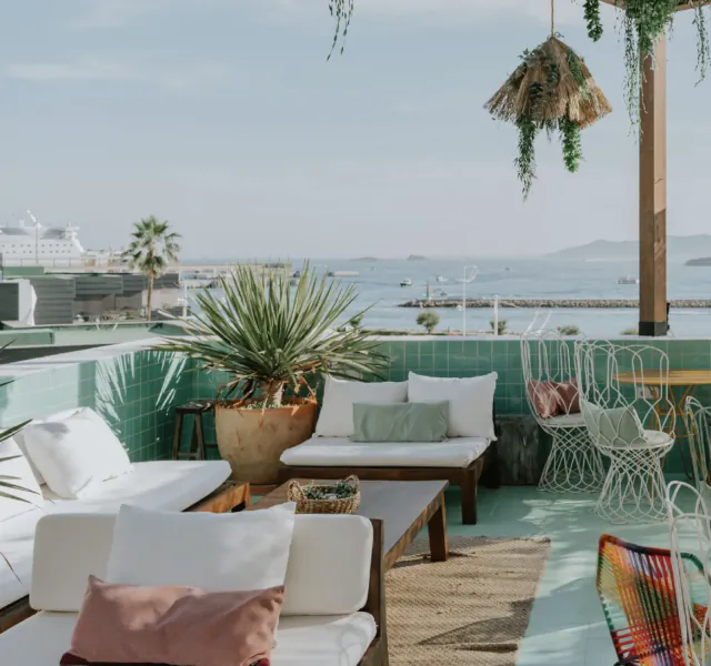 Rooftop terrace with white lounge seating, green tiled walls, potted plants, and sea view
