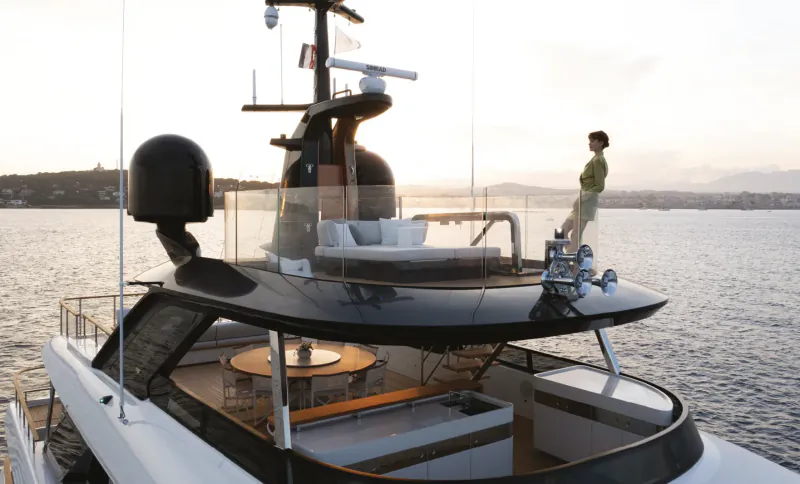 Woman in green blazer standing on the flybridge of a luxury yacht at sunset overlooking calm water