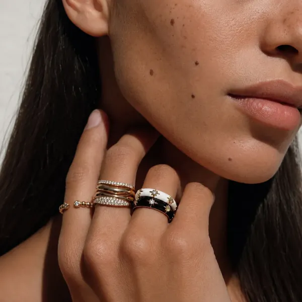 Close-up of a woman’s hand resting on her neck, wearing stacked gold, diamond, and black-and-white enamel rings with star motifs