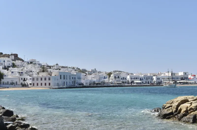 Whitewashed Greek island town with waterfront buildings overlooking turquoise sea under clear blue sky
