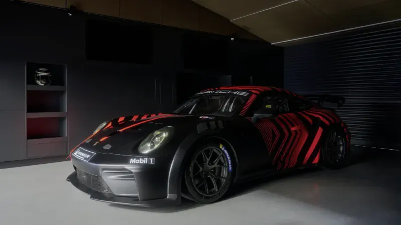 Black Porsche 911 race car with red geometric stripes in a showroom, featuring Mobil 1 and Porsche logos
