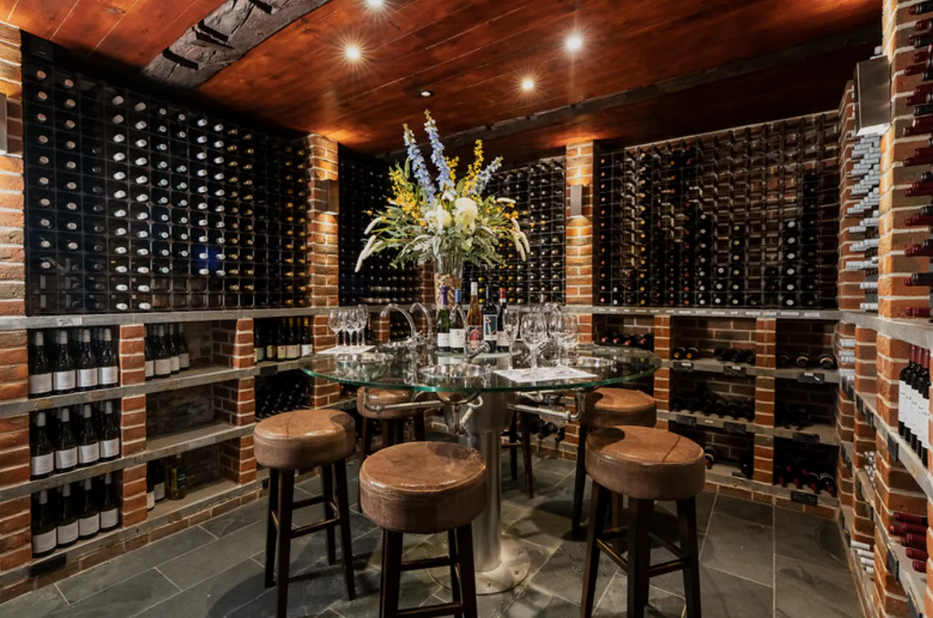 Wine cellar tasting room with round glass table, leather stools, and floor-to-ceiling brick wine racks filled with bottles