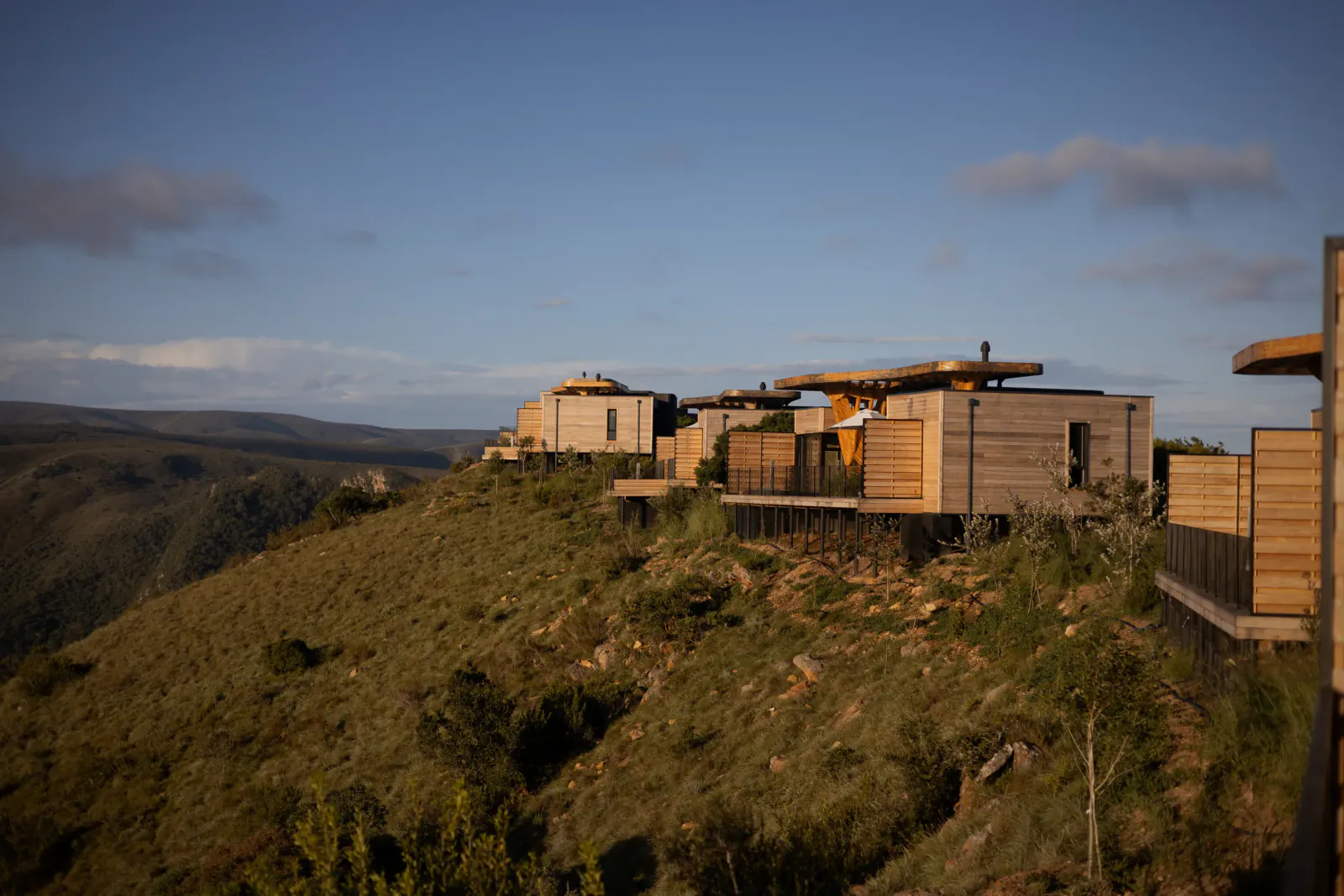 Modern hillside villa with wooden cladding and flat roofs overlooking rolling hills at dusk