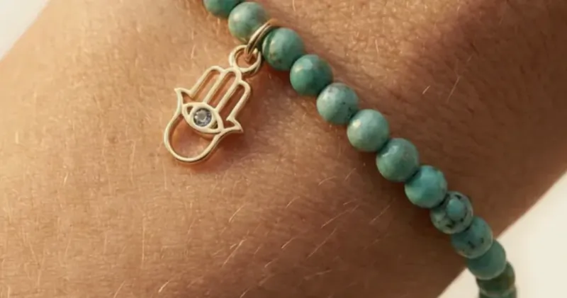 Close-up of a turquoise beaded bracelet with a gold Hamsa hand charm on a wrist