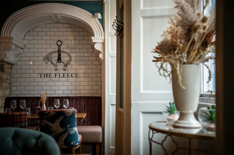The Fleece Cirencester restaurant interior with sheep logo on white tile wall, booth seating, and dried flower vase