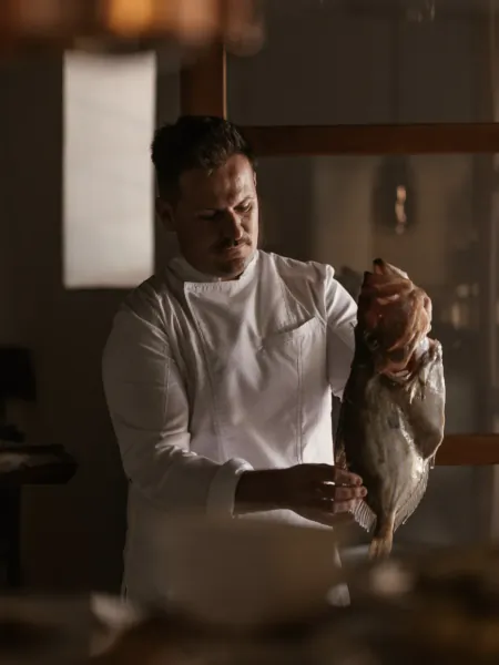 Chef in white uniform holding a large whole fish in a professional kitchen