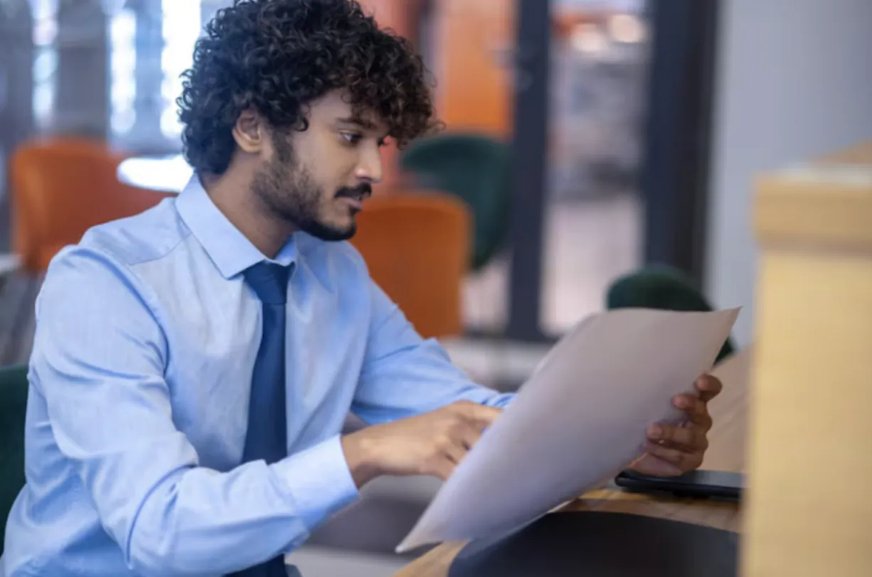 Man in light blue shirt and tie reviewing documents at office desk