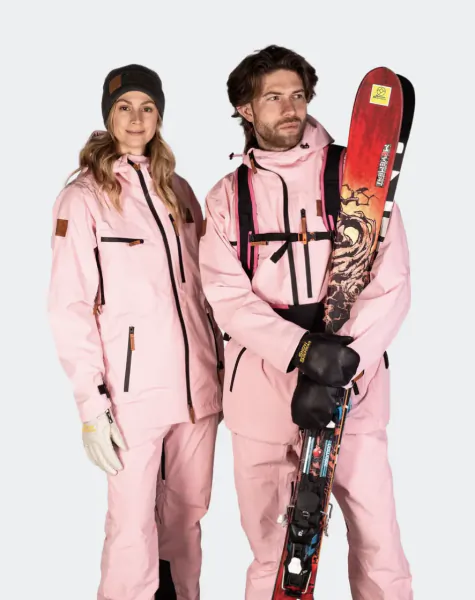 Man and woman in matching pink snow suits pose with skis; man holds red ski with dragon graphic