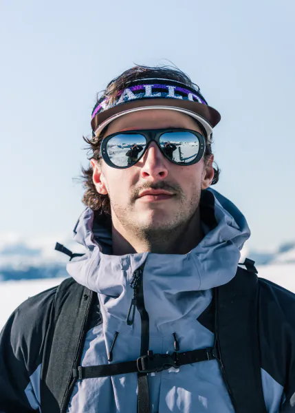 Man in snow wearing VALLON visor sunglasses and light blue jacket with backpack