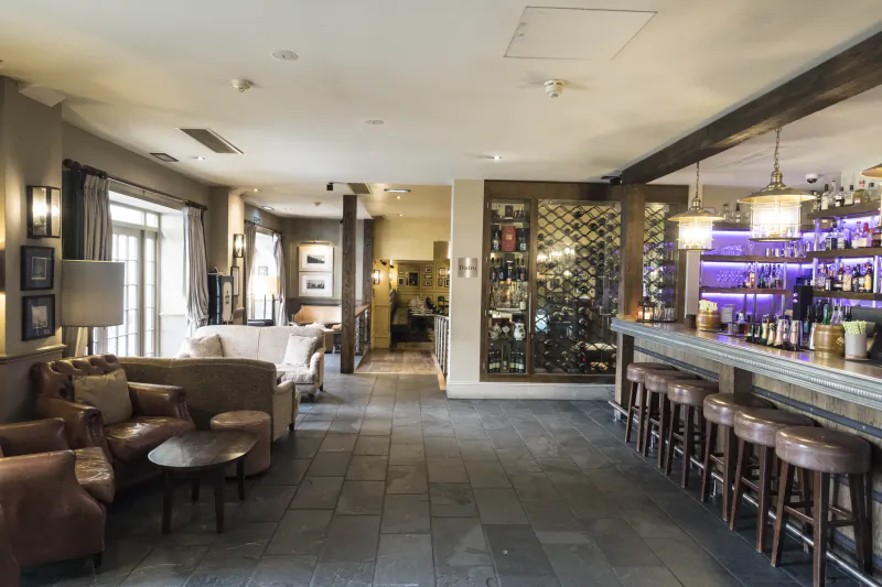 Hotel bar lounge with brown leather sofas, stone floor, and long wooden bar with stools